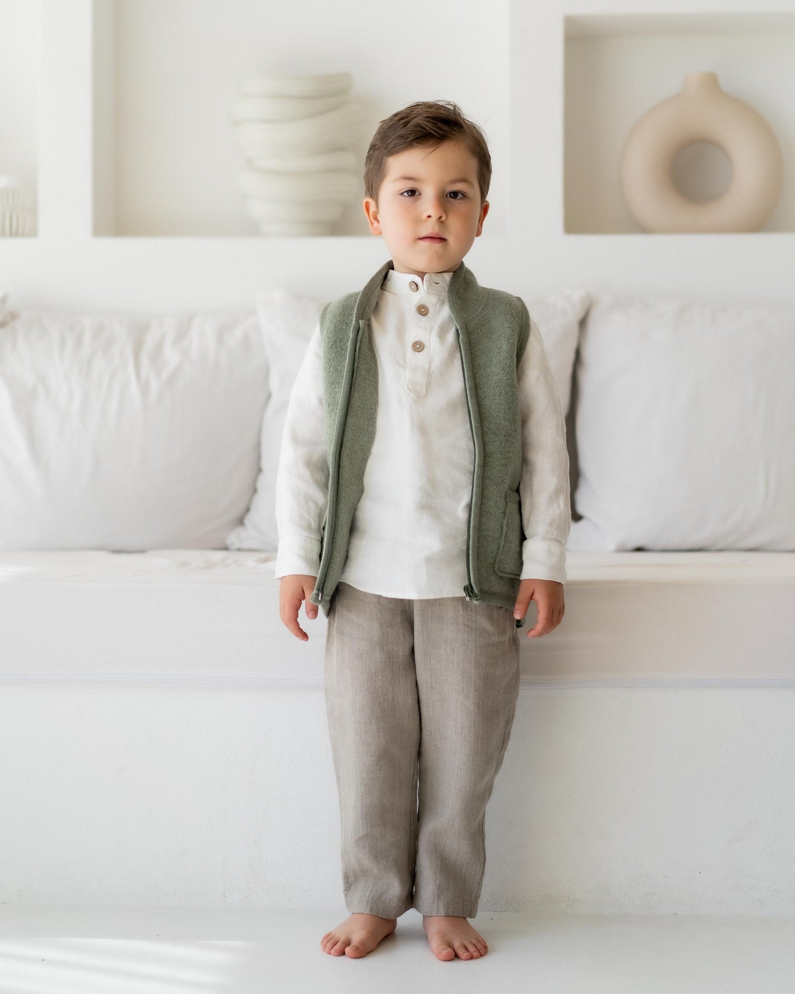 Kind mit Walkweste in Sage vor Couch