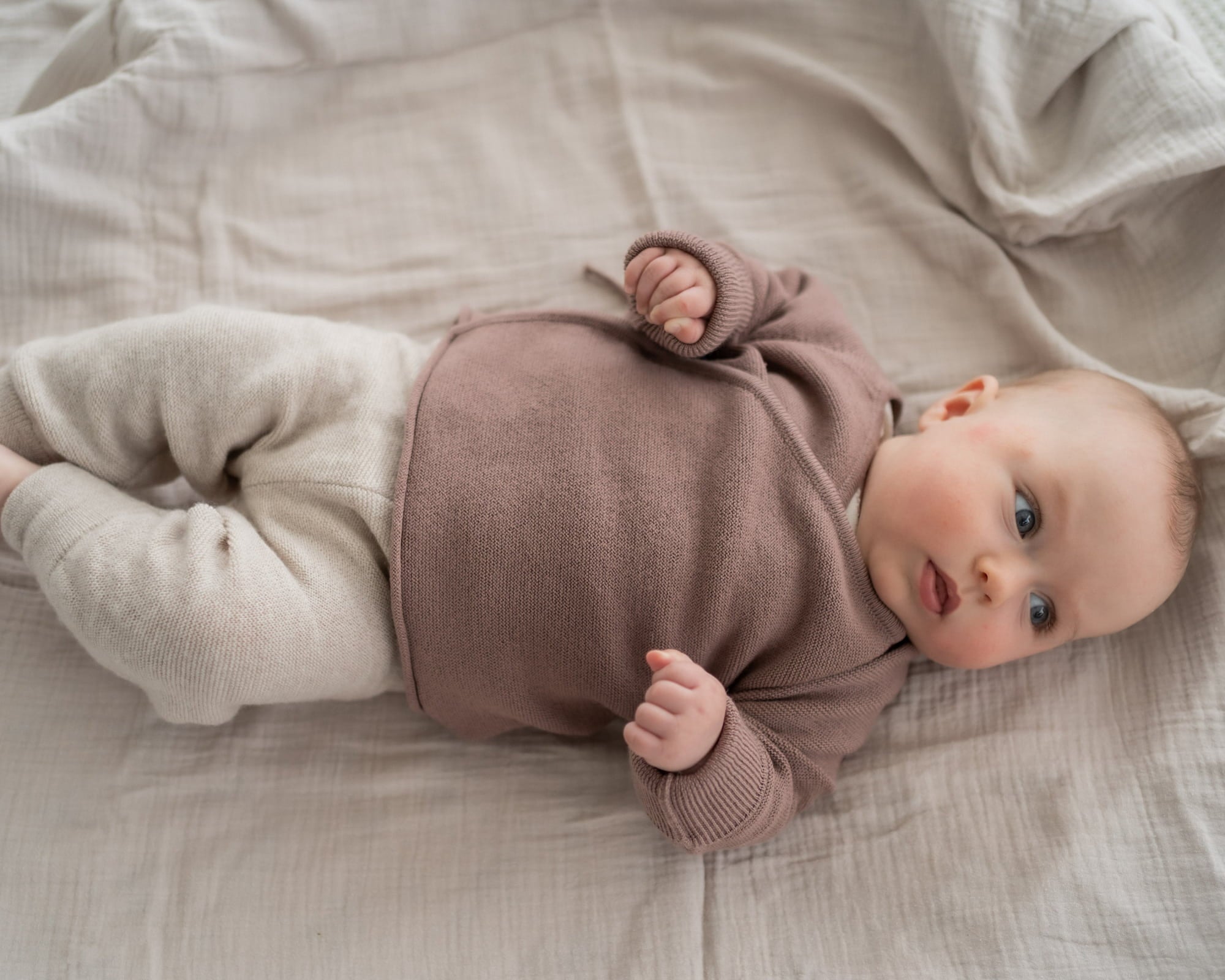 Baby mit Wickeljacke aus Merinowolle liegt auf Decke