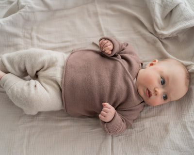 Baby mit Wickeljacke aus Merinowolle liegt auf Decke